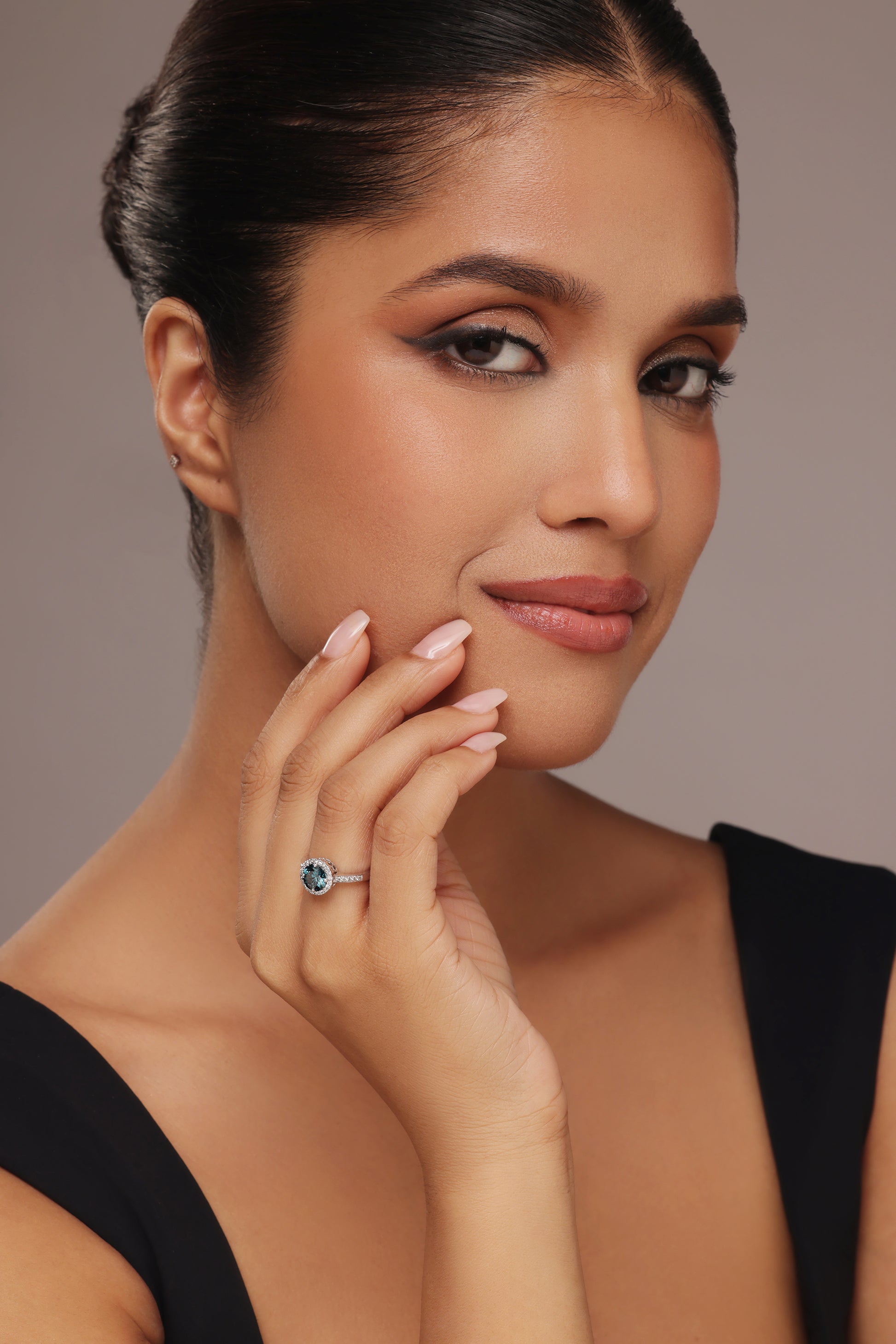 Close-up shot of a hand modeling a ring featuring a vibrant blue stone center, encircled by a round halo of lab grown diamond in it, and set on a round pave band.