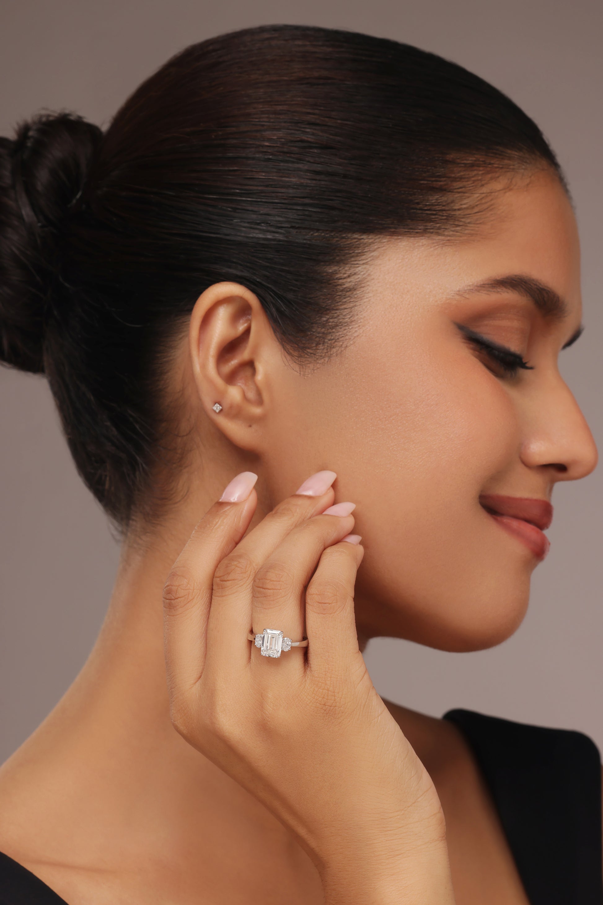 Close-up portrait of a woman modeling a three-stone lab grown diamond in it ring, featuring a center emerald cut and side oval cut diamonds.