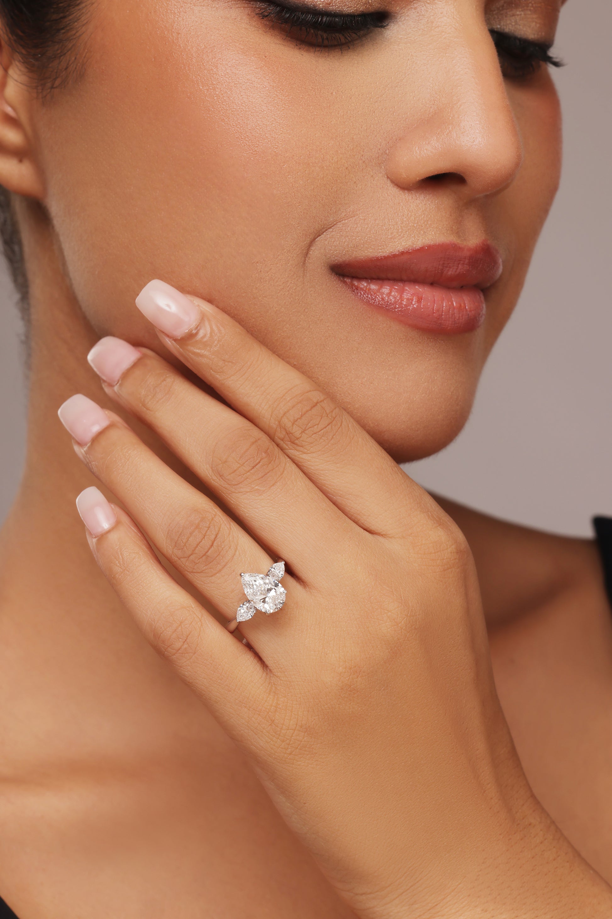Close-up shot of a hand modeling a female diamond ring with lab grown diamond in it, featuring a prominent pear cut center stone flanked by smaller pear-shaped accent diamonds on a simple band.