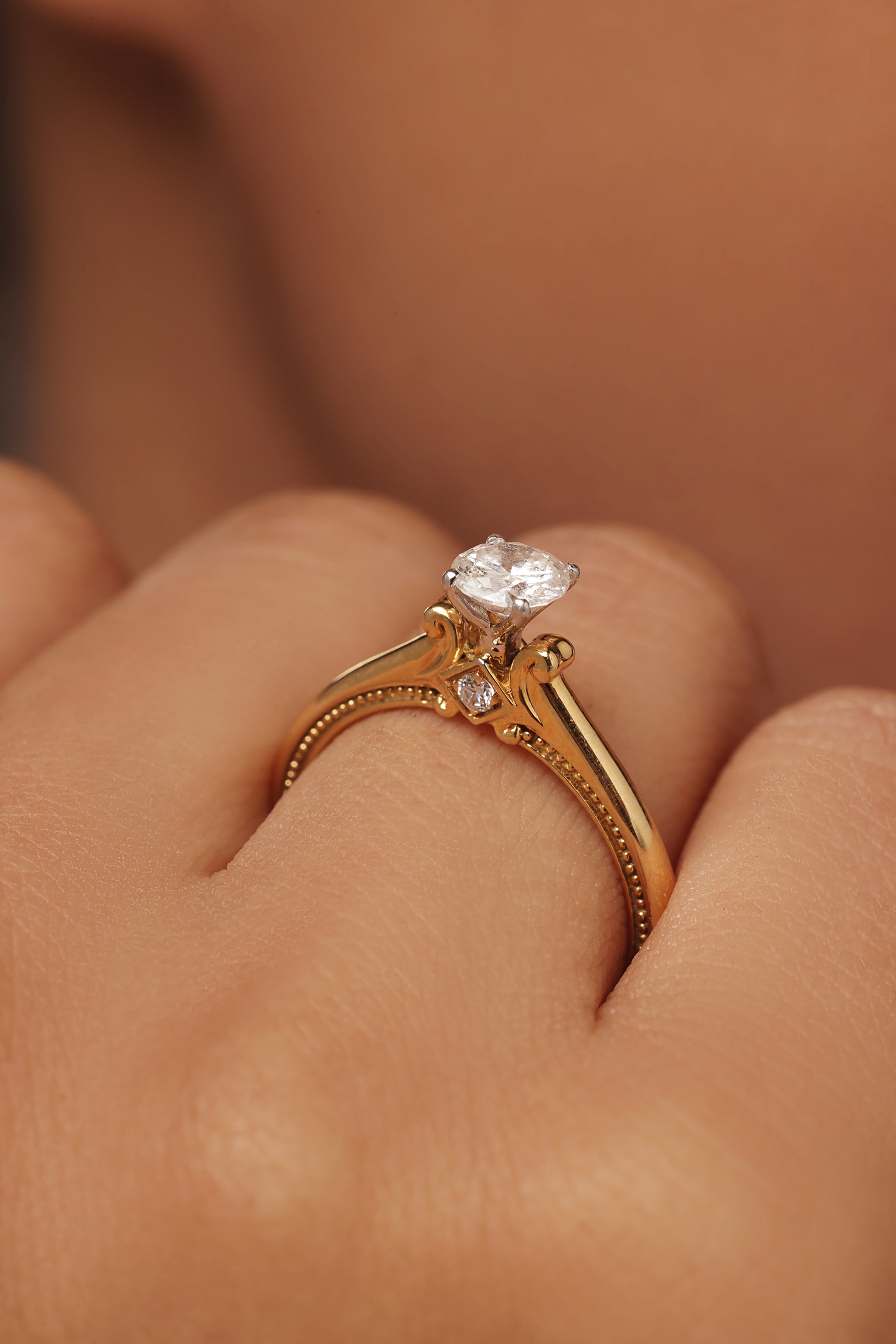 Close-up of a hand modeling a yellow gold round solitaire ring with lab grown diamond in it. The intricate antique-style setting features delicate scrollwork and a small round diamond accent on the band.