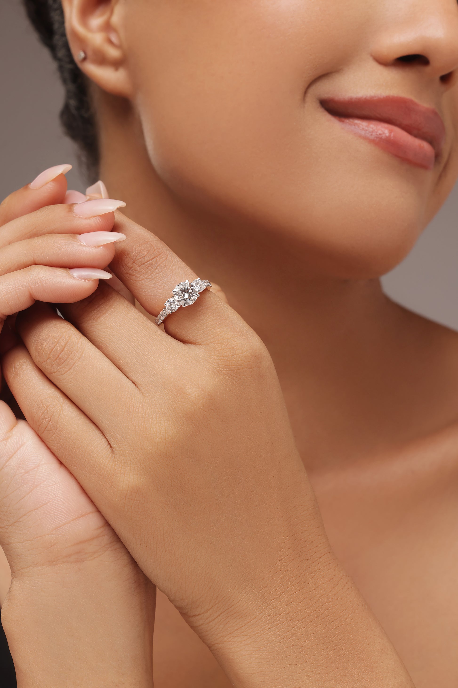 Close-up shot of a woman modeling a lab grown diamond ring featuring a three round solitaire design set on a round diamond pave band with lab grown diamond in it.