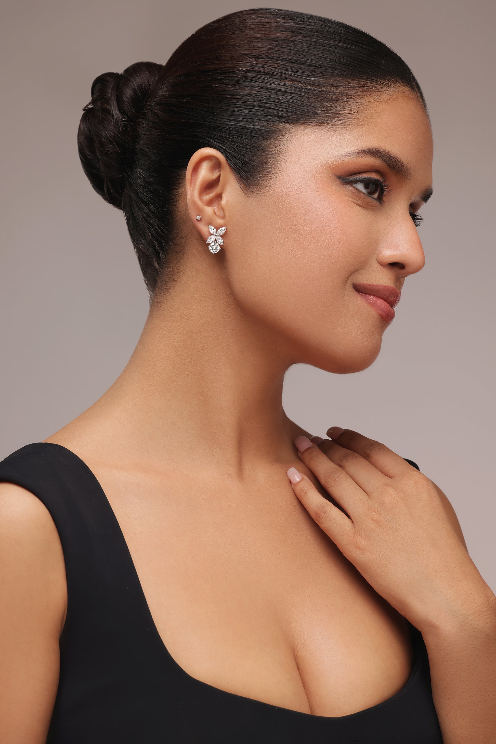 Side portrait of a woman wearing floral-cluster stud earrings with lab grown diamond in it, designed with a combination of pear, round, and marquise diamond shapes, and gently touching her collarbone.