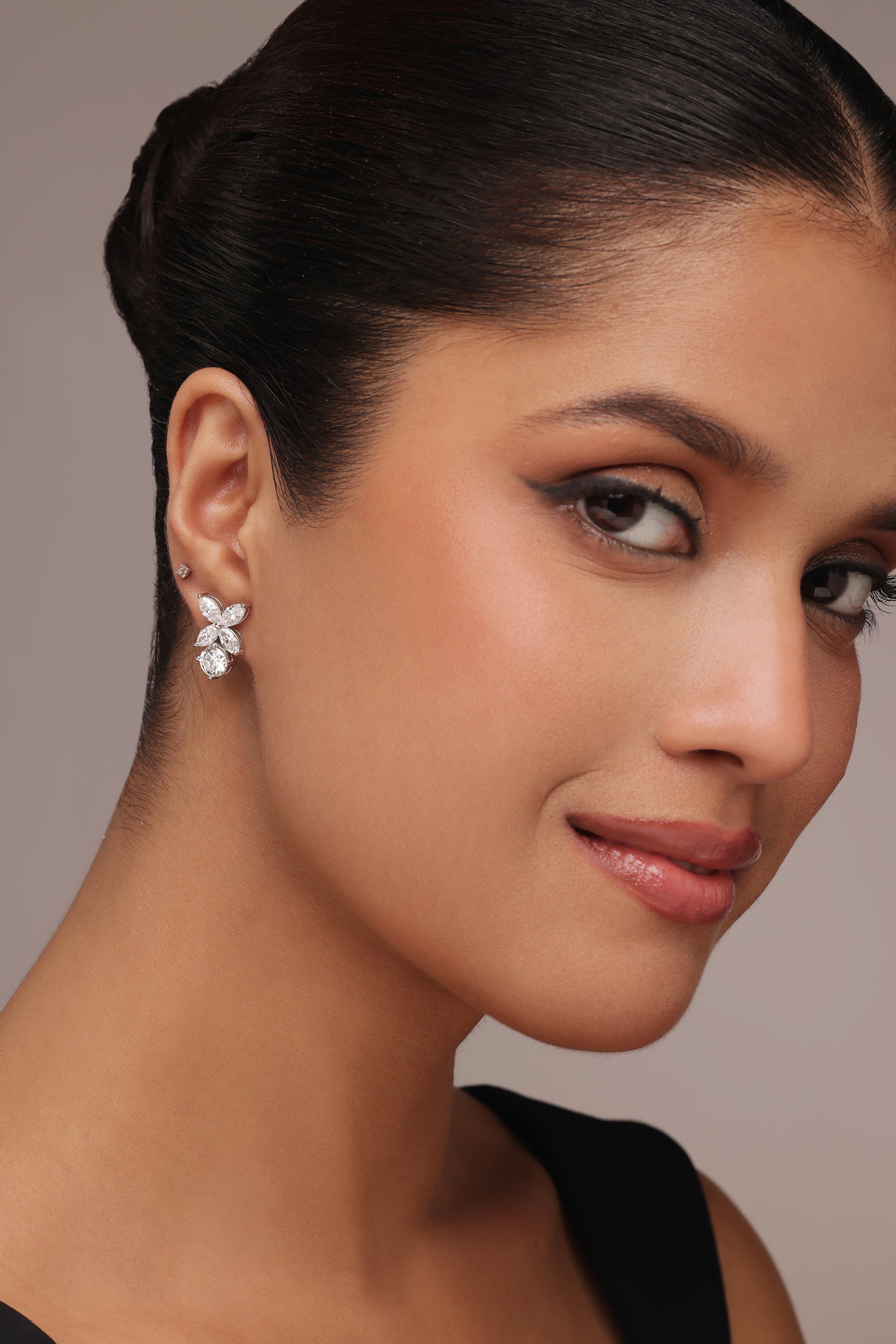 Close-up portrait of a woman wearing floral-cluster stud earrings with lab grown diamond in it, designed with a combination of pear, round, and marquise diamond shapes, in two different poses.