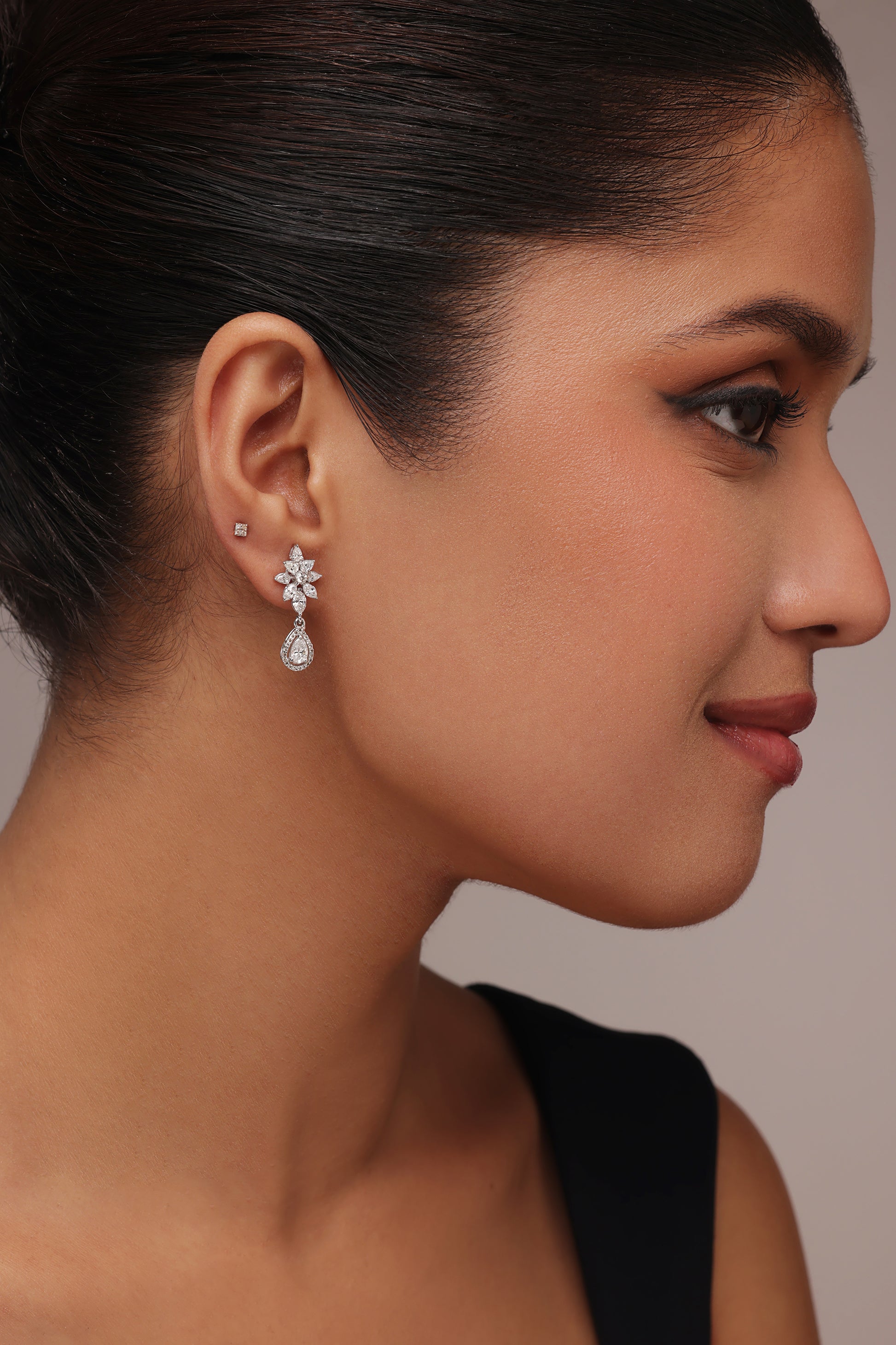 Close-up side profile of a woman modeling drop earrings with lab grown diamond in it. The design features a floral cluster stud and a dangling pear-shaped stone, utilizing a combination of pear, round, and marquise diamond cuts.