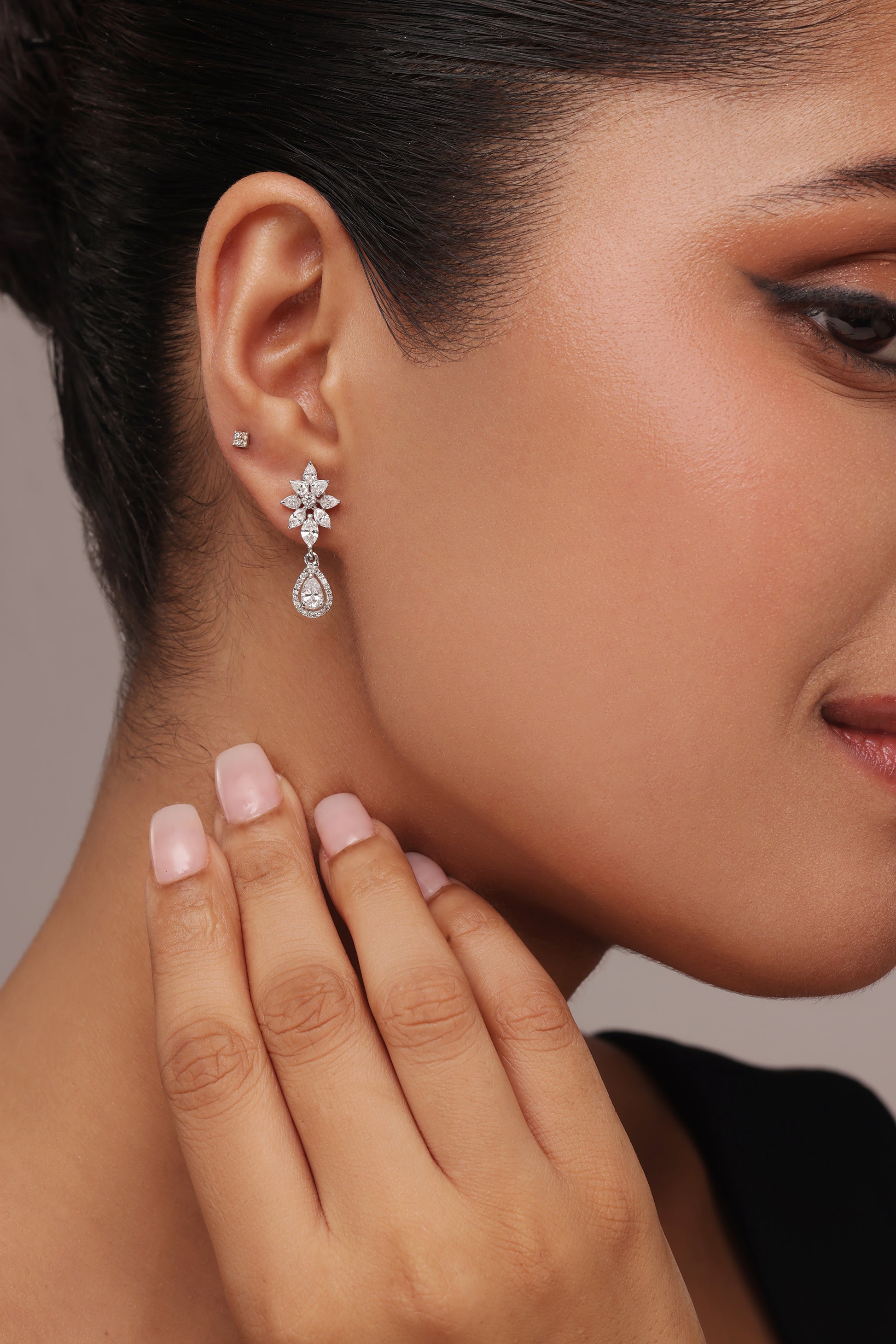 Close-up of a woman modeling elegant drop earrings with lab grown diamond in it. The design features a floral stud and a dangling pear-shaped cluster, utilizing a combination of pear, round, and marquise diamond cuts.