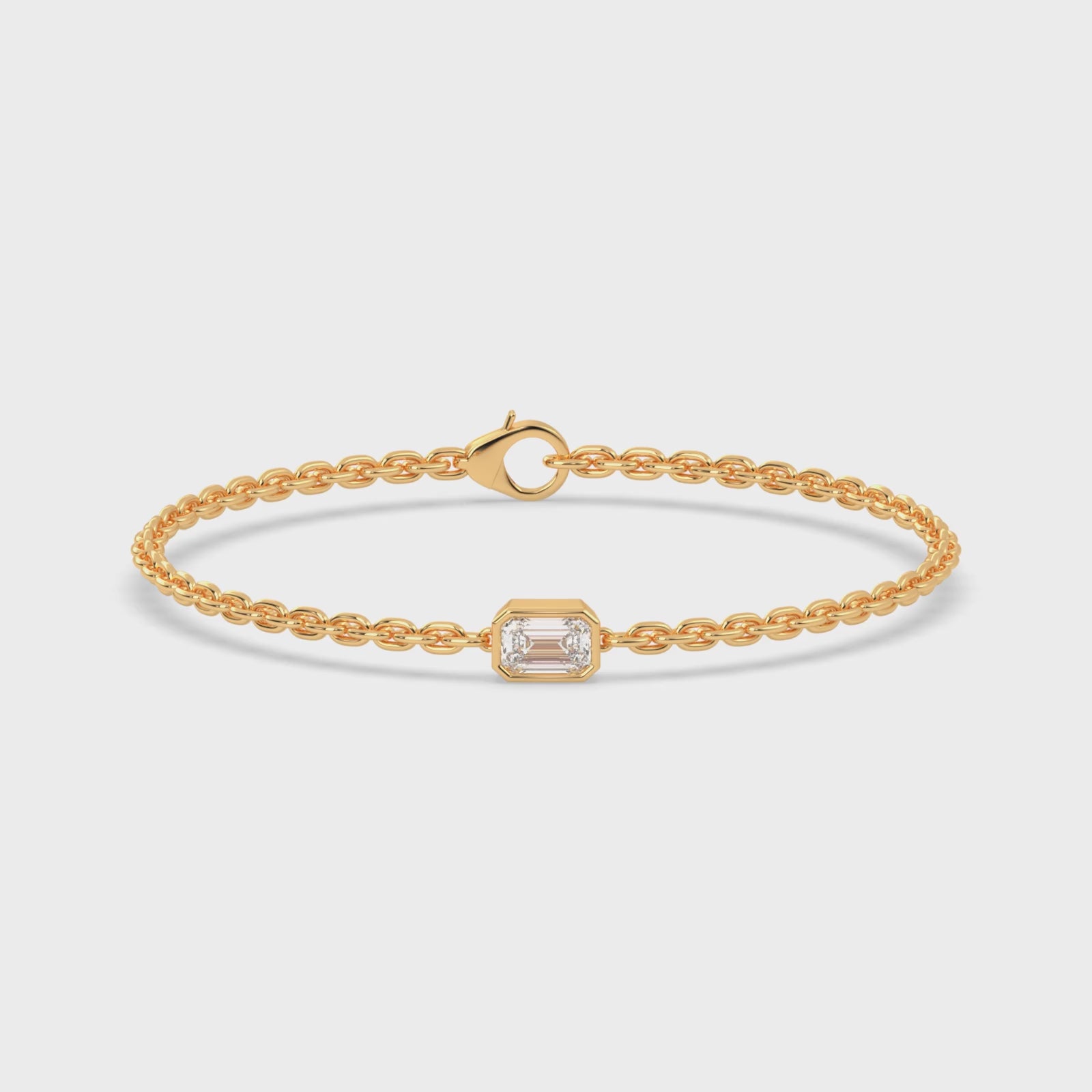 Load video: A yellow gold chain bracelet with a single, horizontally set emerald cut lab grown diamond in it at the center, secured by a clasp.